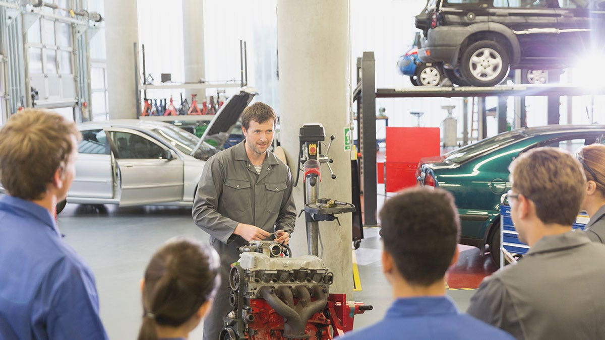 Mechanic explaining car engine to students in auto repair shop