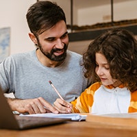 Father helping his son with homework while sitting with laptop Schulstart: Ziele setzen